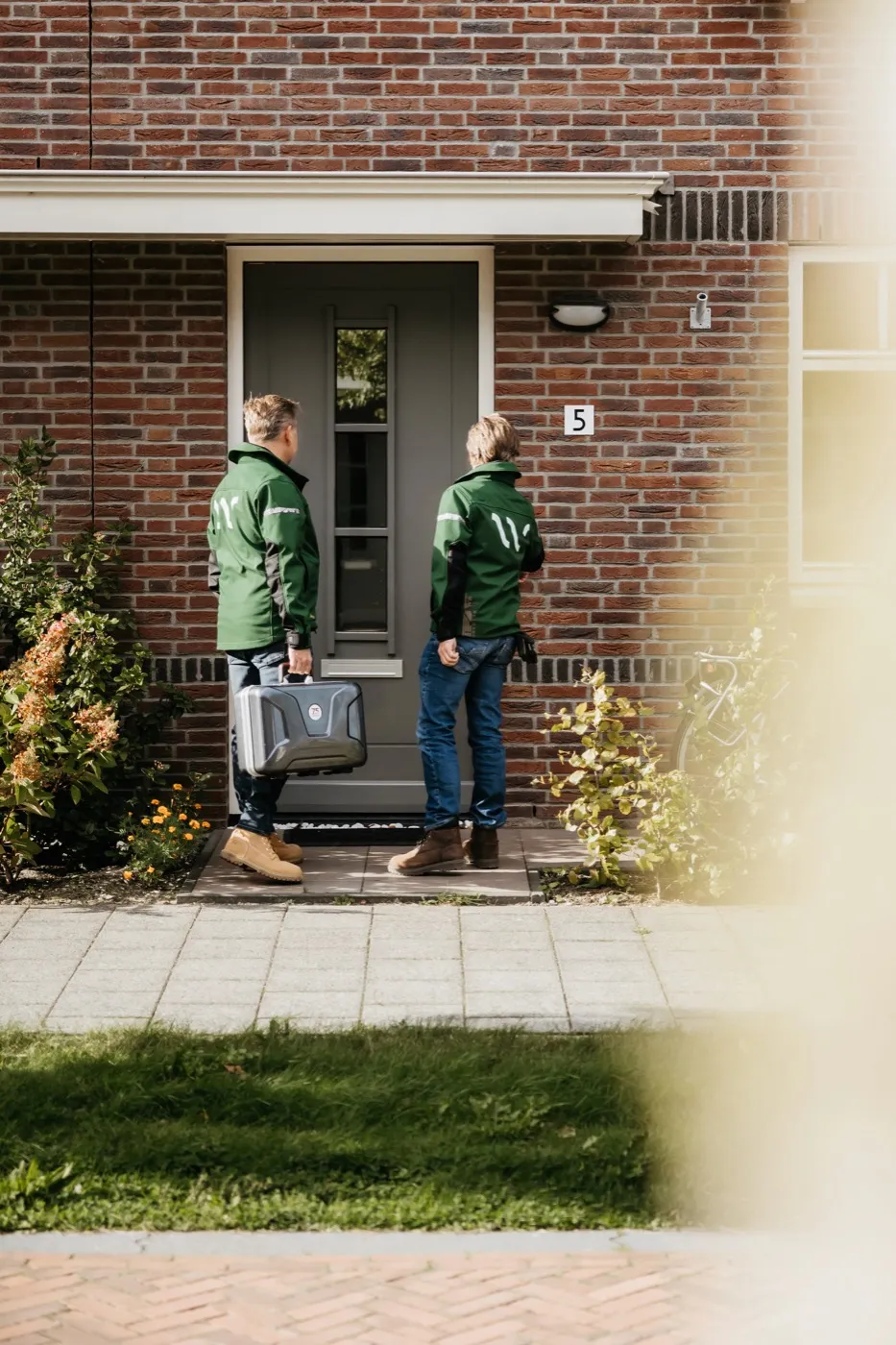 Twee Whspr-installateurs lopen met hun koffer naar de voordeur van een rijwoning